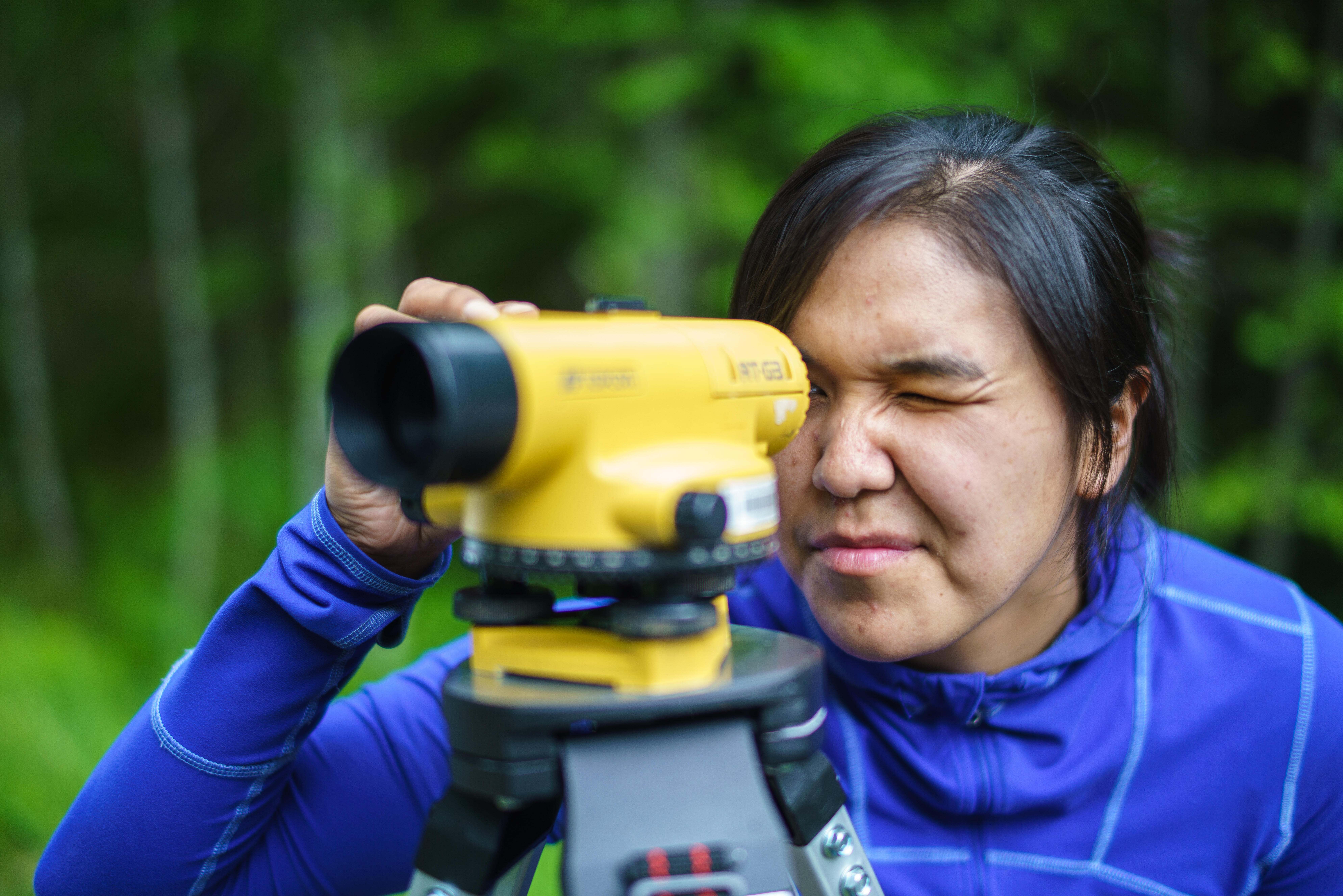 A woman looks through a yellow optical level.