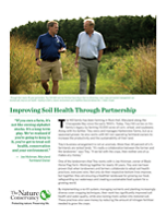 Thumbnail of a factsheet titled Improving Soil Health Through Partnership. The header photo shows two men talking as they walk together down a wide green path cut between tall grasses. 