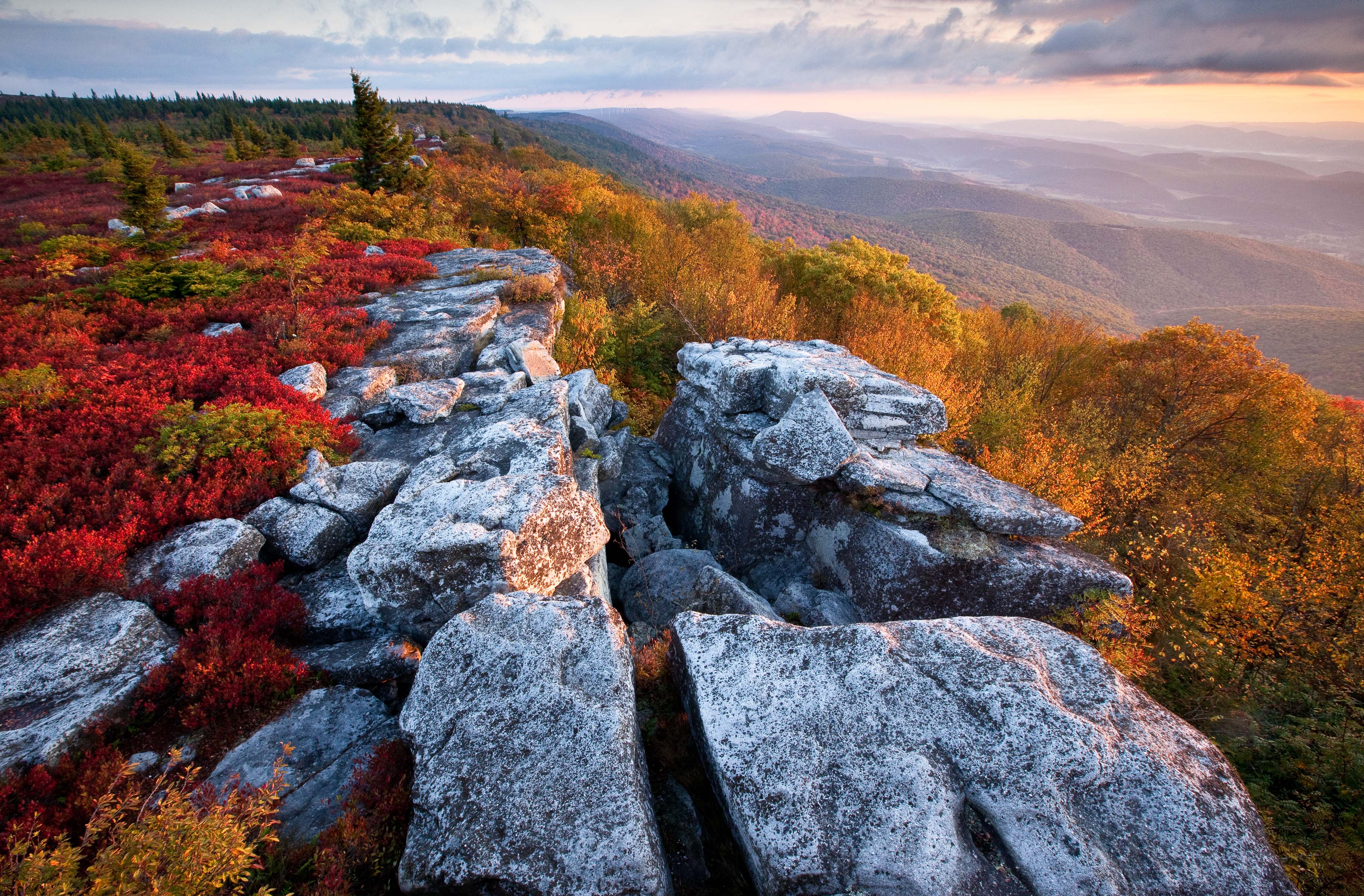 Large rock outcropping dominate the foreground of a view looking out over a mountain ridge and beyond into the mist covered valley.